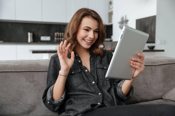 istock Happy lady sitting on sofa looking at tablet and waving. 1350822192