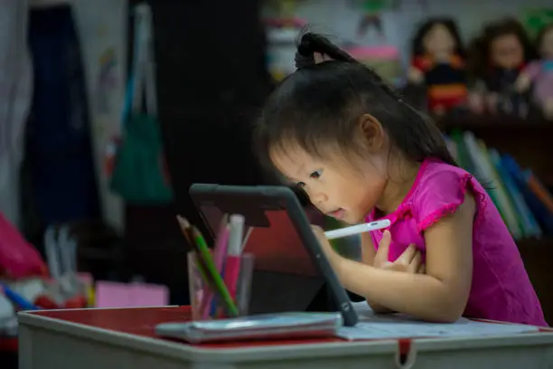 Online education concept. Online class. Asian little girl studying at home. kid in living room at home and using digital tablet to draw.