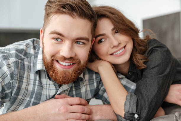 istock Cheerful loving couple sitting on sofa indoors and looking aside. 1350822721