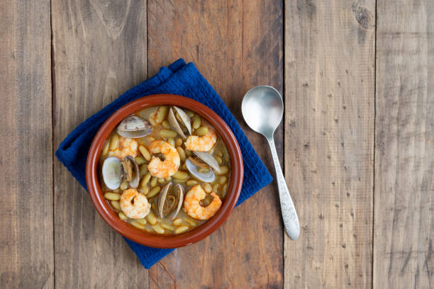 Fabas verdinas with shrimps and clams on a wood background. Copy space. Green beans with prawns and clams in earthenware casserole on wood background. Copy space. top view. fabes stock pictures, royalty-free photos & images