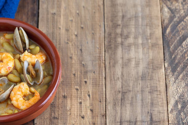 Green beans with prawns and clams in earthenware casserole on wood background. Copy space. top view. Fabas verdinas with prawns and clams in an earthenware casserole on a wooden base. Copy space. super view fabes stock pictures, royalty-free photos & images