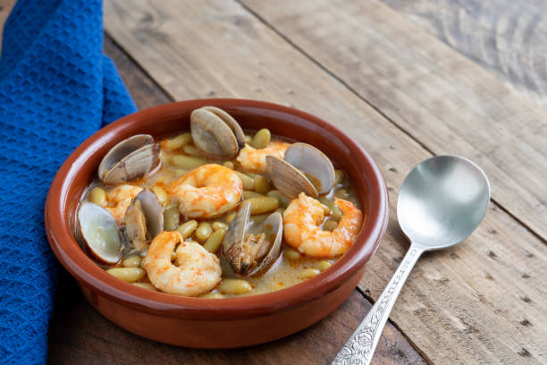 Green beans with prawns and clams in earthenware casserole on wood background. Copy space. top view. Fabas verdinas with prawns and clams in an earthenware casserole on a wooden base. Copy space. super view fabes stock pictures, royalty-free photos & images