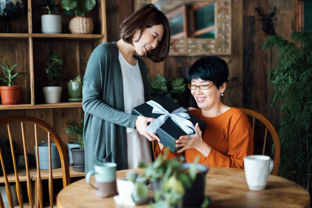 A senior Asian mother receiving a present from her daughter at home. The love between mother and daughter. The joy of giving and receiving stock photo