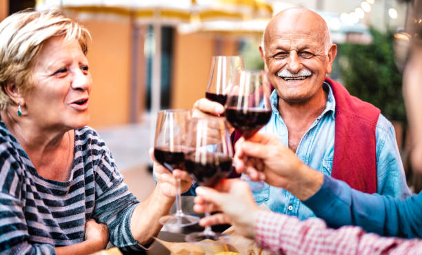 glückliches seniorenpaar, das spaß beim trinken von rotwein mit freunden auf der dinnerparty hat - rentner essen zusammen auf dem balkon des restaurants - lebensstilkonzept auf warmem filter - fokus auf männergesicht - senior adult retirement mature adult couple stock-fotos und bilder