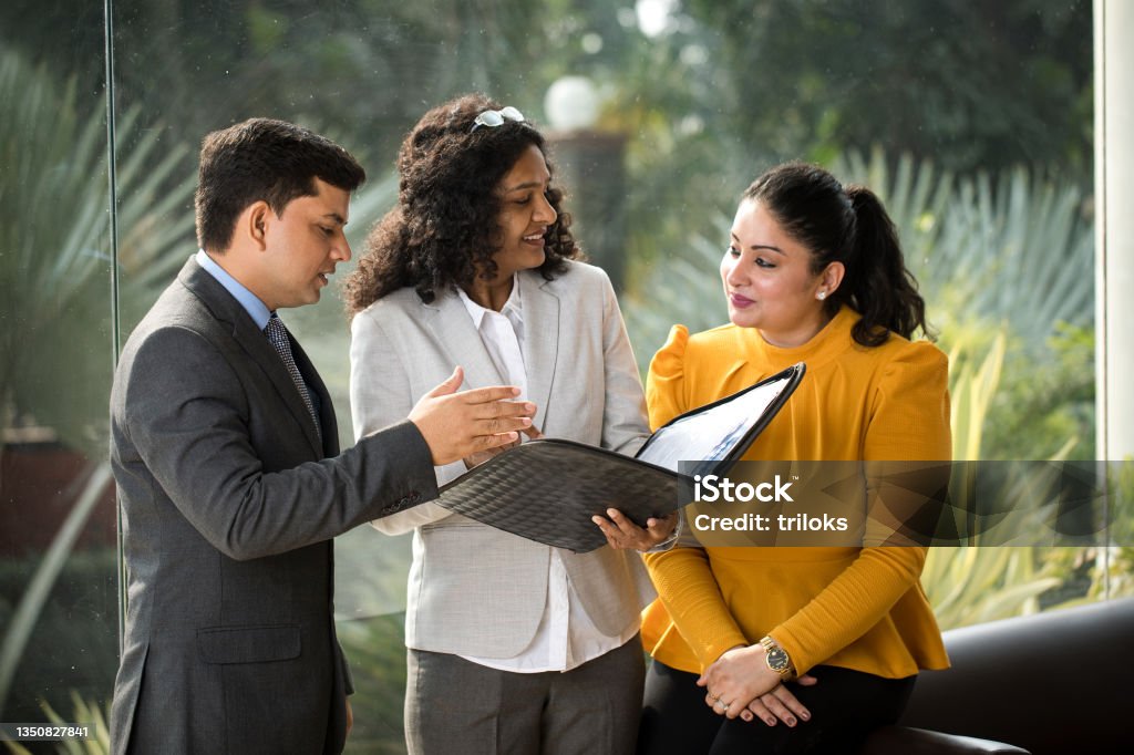 Business colleagues discussing over filed reports at office Businessman and businesswomen discussing over filed documents at office India Stock Photo