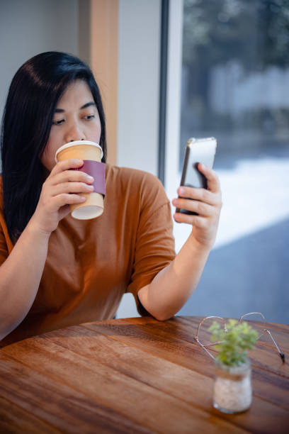istock Woman drinking coffee and using her smart phone at the table by the window in cafe 1350828649