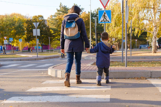 mamá e hijo cruzan la carretera en el paso de cebra. - rules of the road fotografías e imágenes de stock