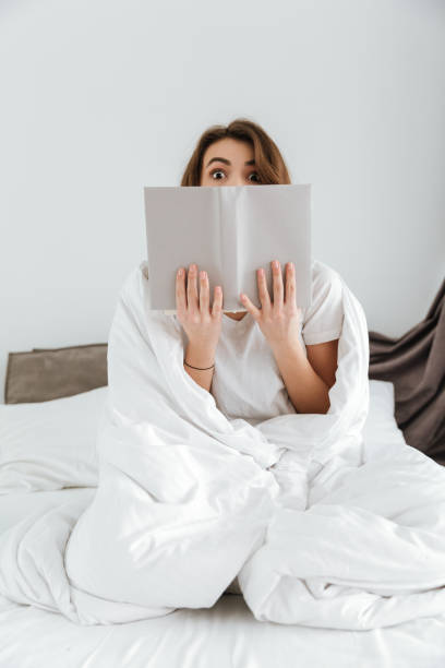 istock Happy woman sitting on bed at home while reading book. 1350830465