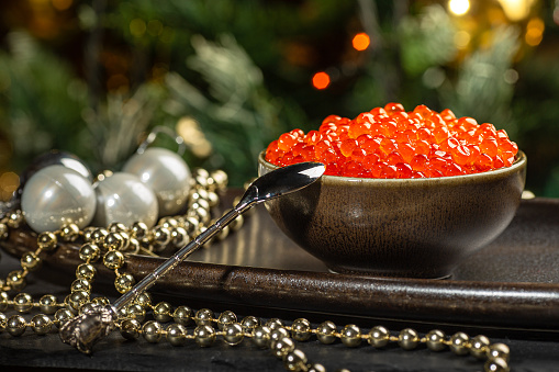 Red caviar in a a ceramic bowl, silver beads and pearls on a silver tray. Christmas and New Year background