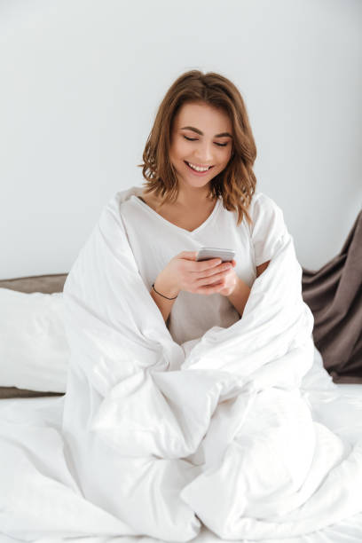 istock Happy beautiful young woman sitting and using mobile phone in bed 1350830948