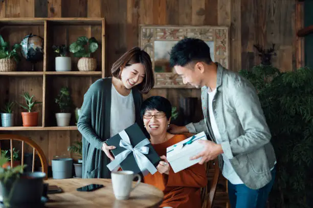 Photo of A senior Asian mother receiving presents from her daughter and son at home. Family love. The joy of giving and receiving