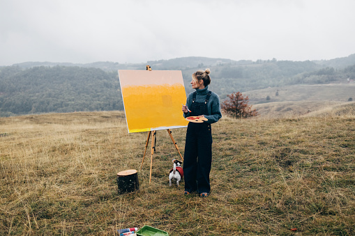 Unrecognizable female artist Â relaxing while painting an art canvas outdoors with her dog