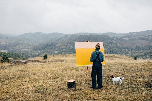 Rear view of unrecognizable female artist Â relaxing while painting an art canvas outdoors with her dog