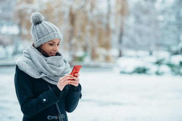 donna che si fa selfie con uno smartphone e indossa una sciarpa e un cappello in una fredda giornata invernale - wind scarf women people foto e immagini stock