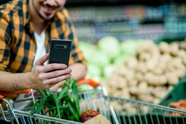 istock Young handsome man in a supermarket using smartphone while grocery shopping 1350836141