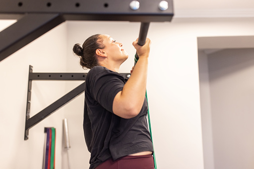 Woman doing pull-ups on a bar at fitness studio. Female exercising in a health club and doing chin-ups.