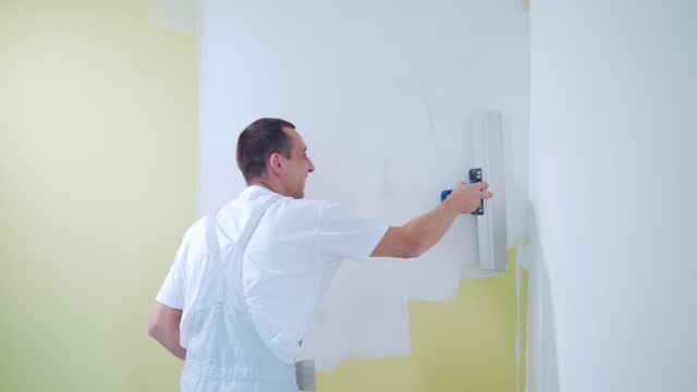 experienced repairman is plastering wall, using spatula, putty knife and white modern mortar, stuccoing