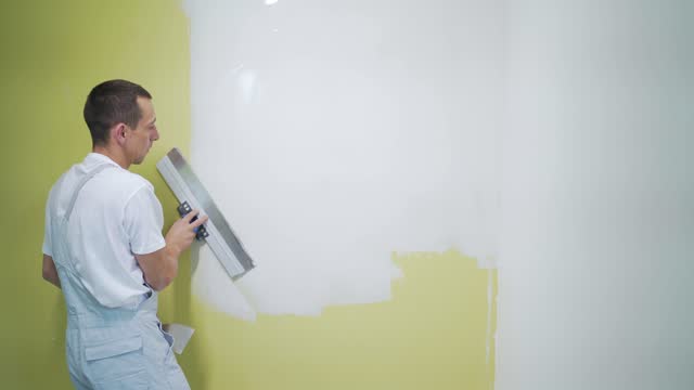 experienced repairman is plastering wall, using spatula, putty knife and white modern mortar, stuccoing