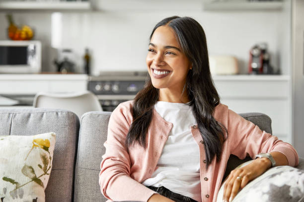 smiling woman looking away while sitting on sofa - one young woman only imagens e fotografias de stock