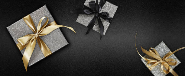 istock Black Friday glittering silver gift boxes wrapped with golden ribbon bow  isolated on black background, template for promotional card with copy space 1350849943