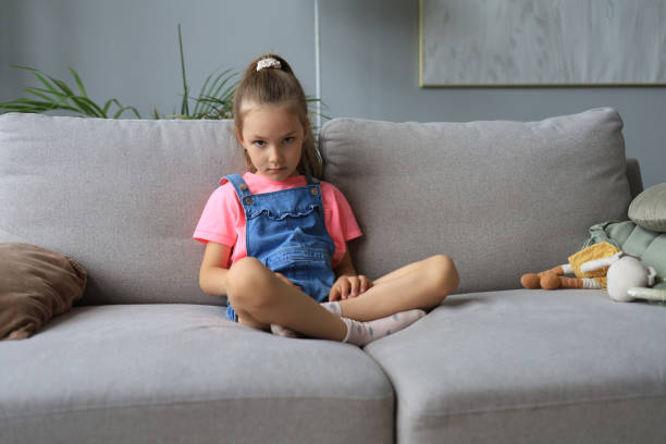 istock Sad little girl sitting on sofa alone at home. 1350852986