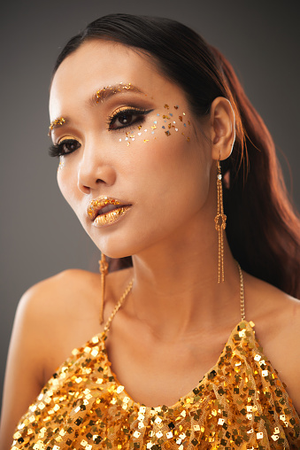Face of calm beautiful young woman in glitter top and black and golden eye make-up