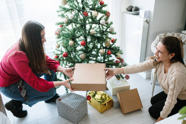 Two women placing presents under a Christmas tree