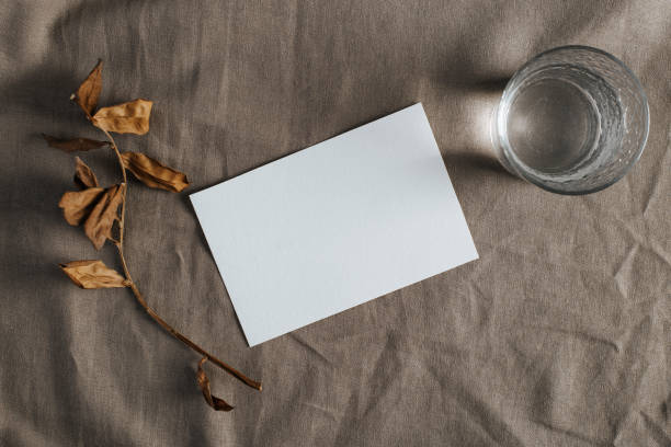 istock Autumn seasonal rustic composition layout. White card mock up with empty space for message, dry sprig and glass of water on textile background. Top view, flat lay 1350854835