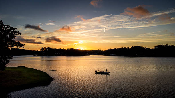 Fisherman on boat fishing at Sunrise Fisherman silohetted in front of an early morning sunrise sky fishing out of his bass boat during a summer sunrise on lake hamilton in arkansas. Photo taken from Drone. fishing boat stock pictures, royalty-free photos & images