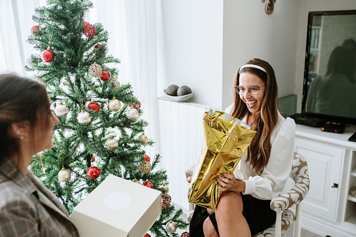 Young women exchanging presents by a Christmas tree at home