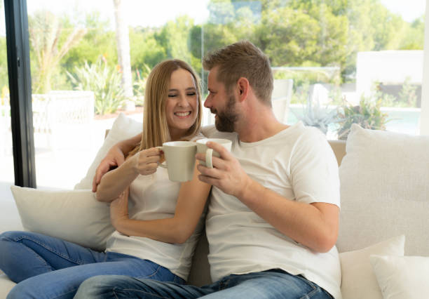 istock Young couple holding cup of coffee while embracing in sofa 1350855703
