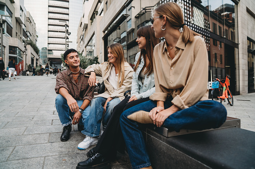 Four friends are talking together in the city. They are sitting in a modern district.