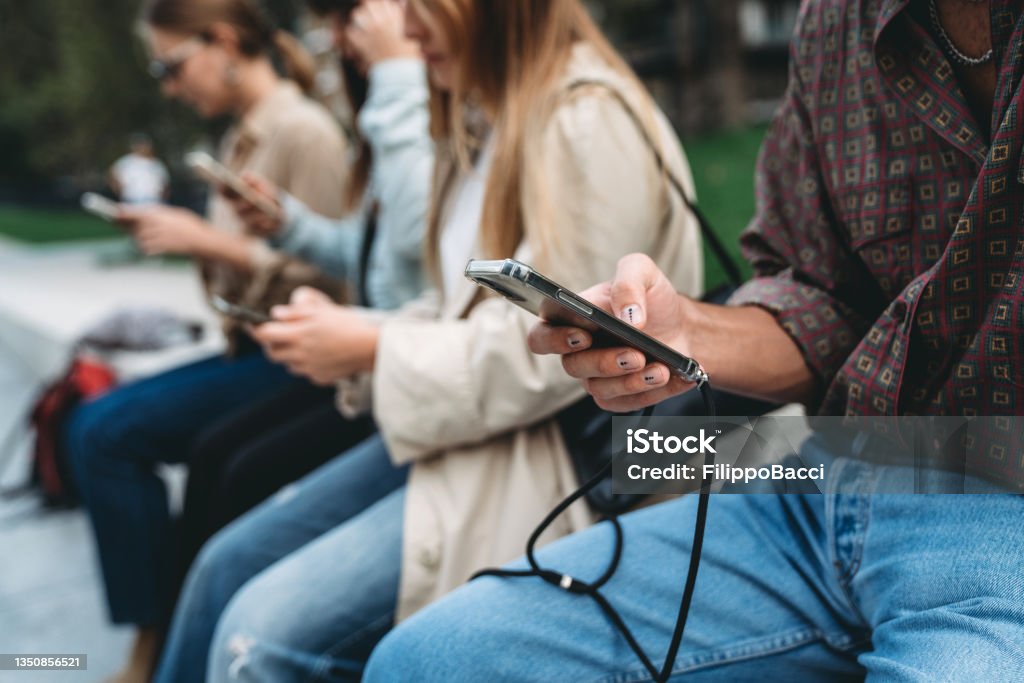 Vier Freunde benutzen Smartphones, während sie in einem öffentlichen Park in der Stadt sitzen - Lizenzfrei Fake News Stock-Foto