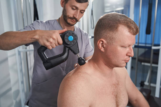 istock Specialist massages back with percussion tool of man with disability 1350856779