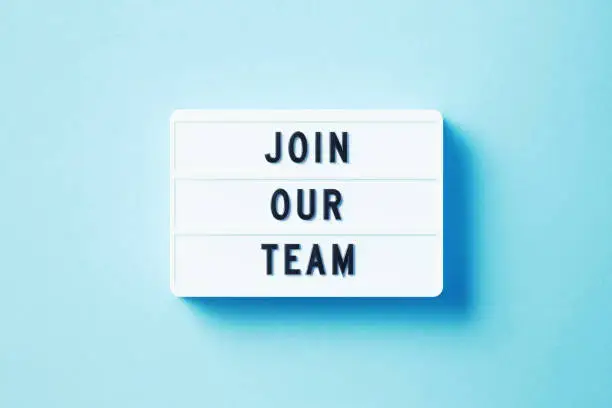 Join Our Team written white lightbox sitting on blue background. Horizontal composition with copy space. Recruitment concept.