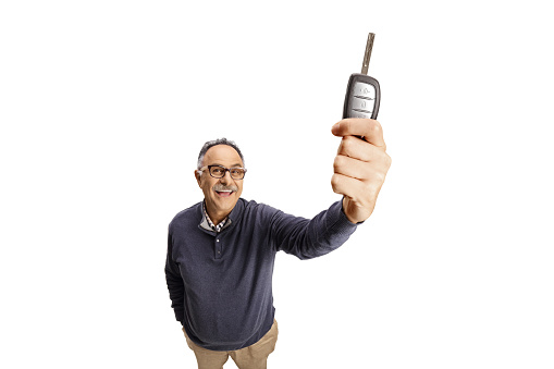 Casual mature man holding a car key in front of camera isolated on white background