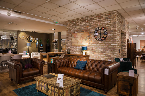 A wide-angle view of a department store in Newcastle upon Tyne. The furniture is placed and styled like a real-life living room and there is a large clock on the bricked wall on the shop floor.