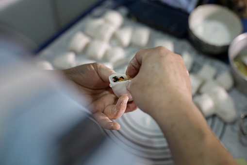 An Asian woman is folding stuffed 'jiaozi' at home.