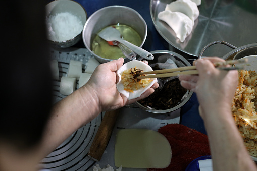 An Asian woman is adding crispy fried shallot on jicama 'jiaozi' at home.