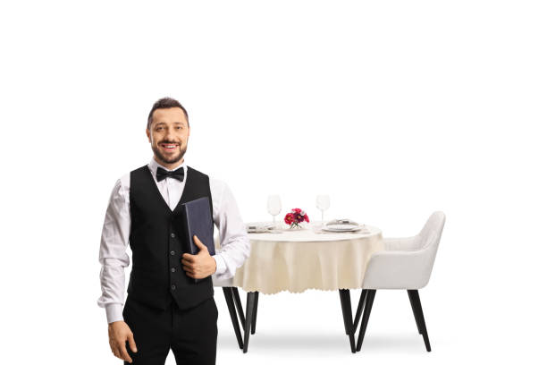 istock Waiter with a bow tie holding a menu list in front of a restaurant table 1350861656