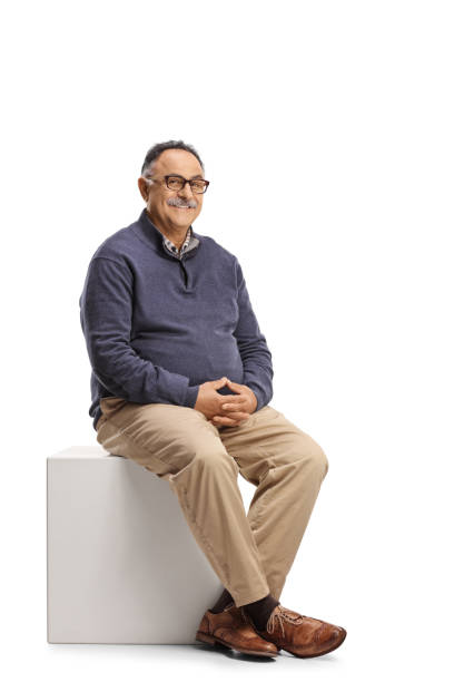 istock Mature casual man sitting on a white cube 1350861660
