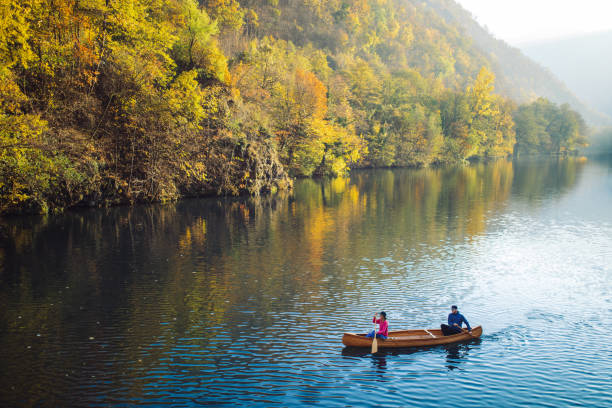 A man paddes a canoe on a lake in Vermont during fall foliage season. Summer cabins line the shore in the background.