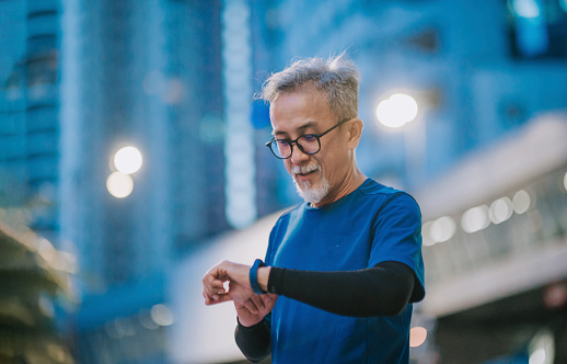 Asian chinese senior man checking his heartbeat with fitness tracker after running in the city during late evening