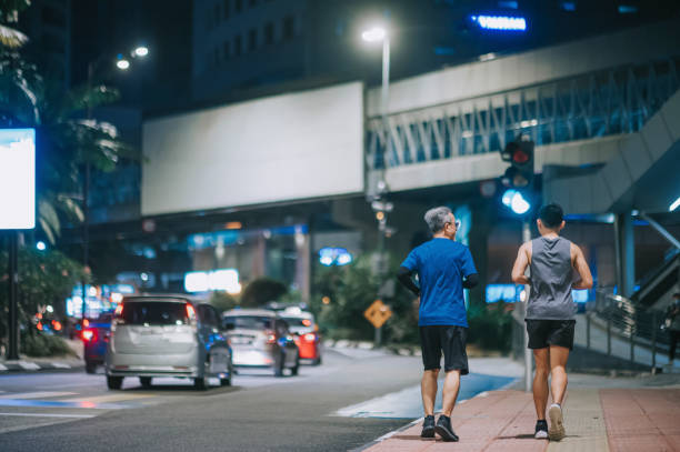rear view asian chinese active senior man and his son running jogging in the city at night after work together - outdoors adult child sport imagens e fotografias de stock