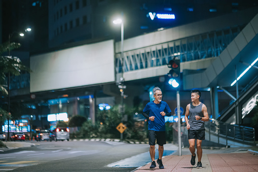 Asian Chinese active senior man and his son running jogging in the city at night after work together