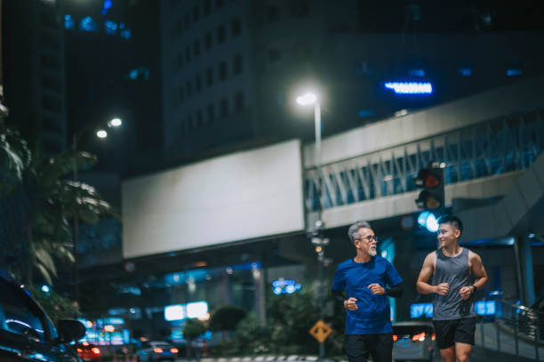 asian chinese active senior man and his son running jogging in the city at night after work together - outdoor pursuit fotos imagens e fotografias de stock