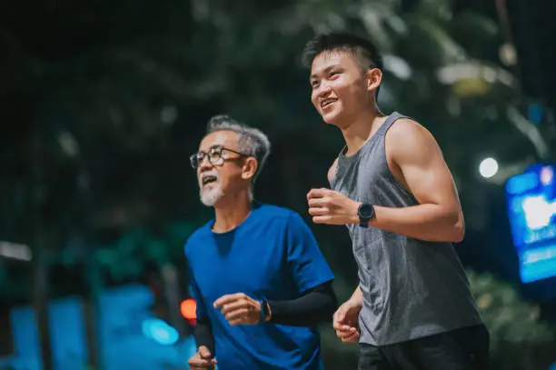 Photo of Asian Chinese active senior man and his son running jogging in the city at night together