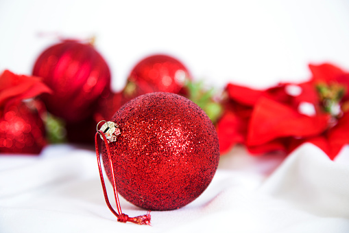 Red glitter Christmas tree ornaments and poinsettia on white background.