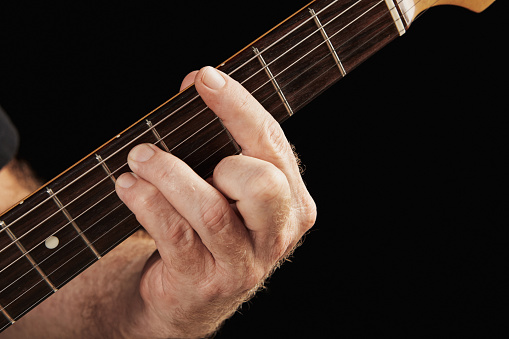 Male hand fingering a shape on an electric guitar fretboard.