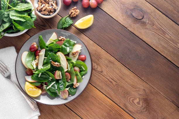 istock Healthy spinach salad made with red apple, wallnuts, grapes. Wooden rustic background, top view 1350870774